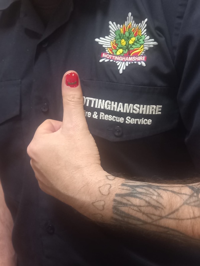 A firefighter in Nottinghamshire Fire and Rescue Service uniform giving a thumbs up, a single thumbnail painted red with a smiley face on it