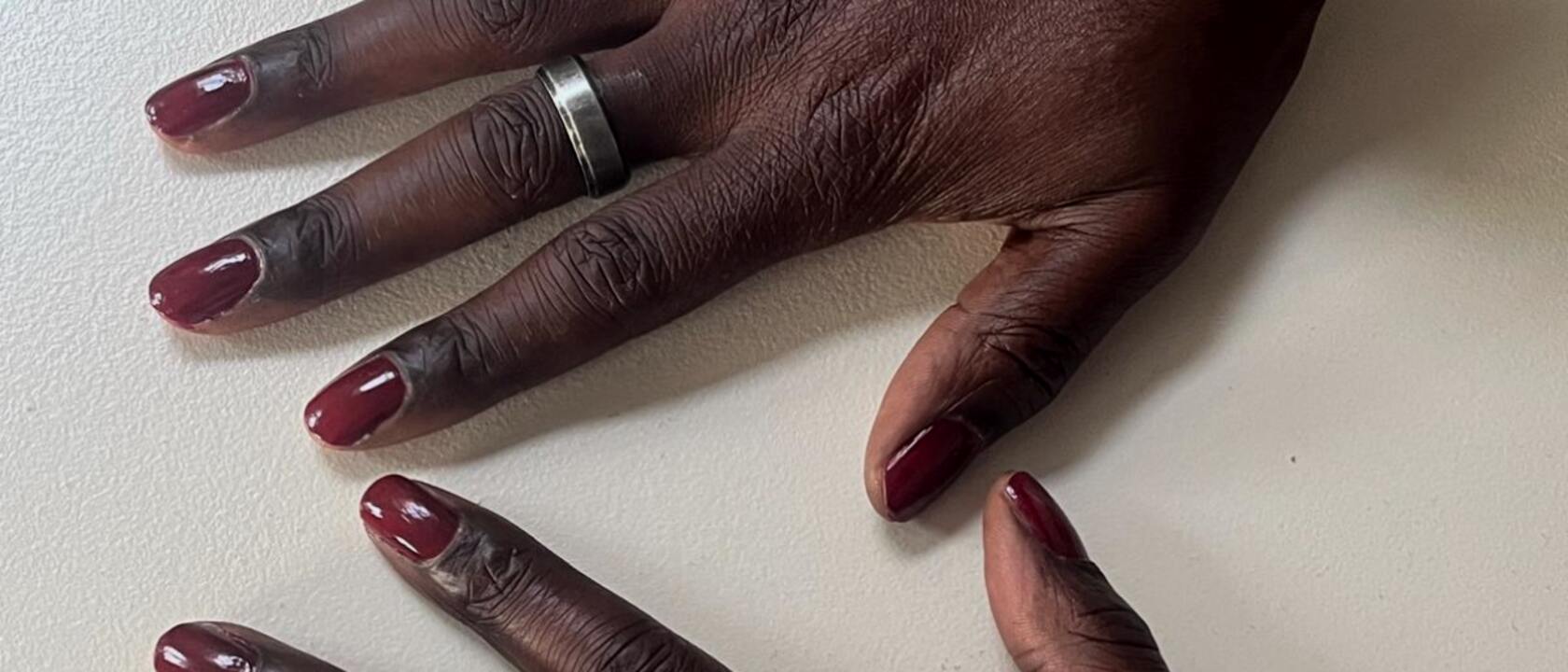 Weathered hands with deep oxblood painted nails, flat on a table