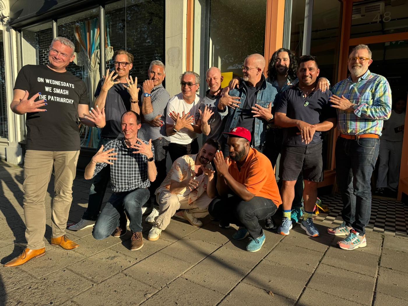A group of men outside a salon, laughing, holding up freshly painted nails.