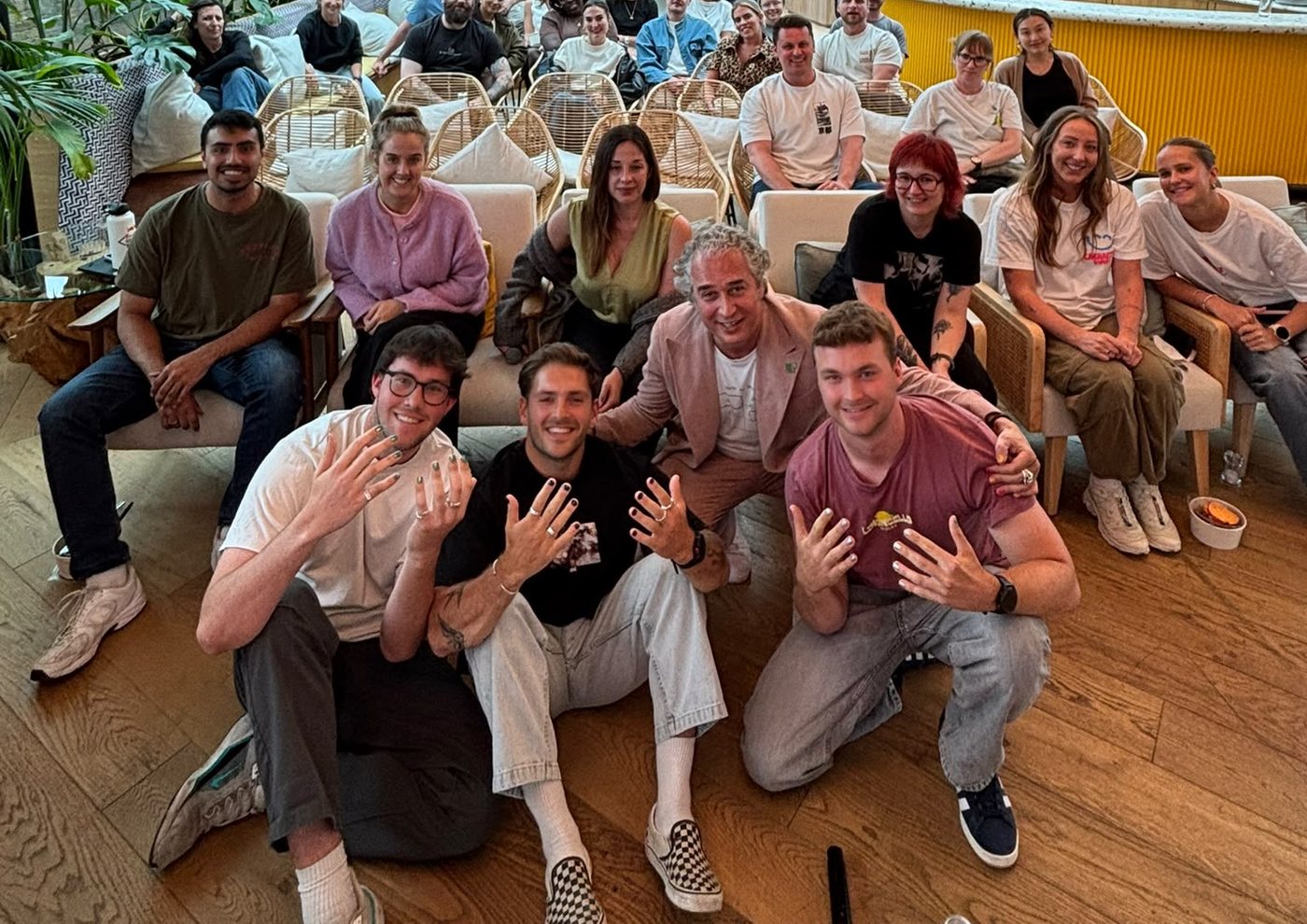 A workplace team gathered in their own office, four colleagues at the front holding up their painted nails