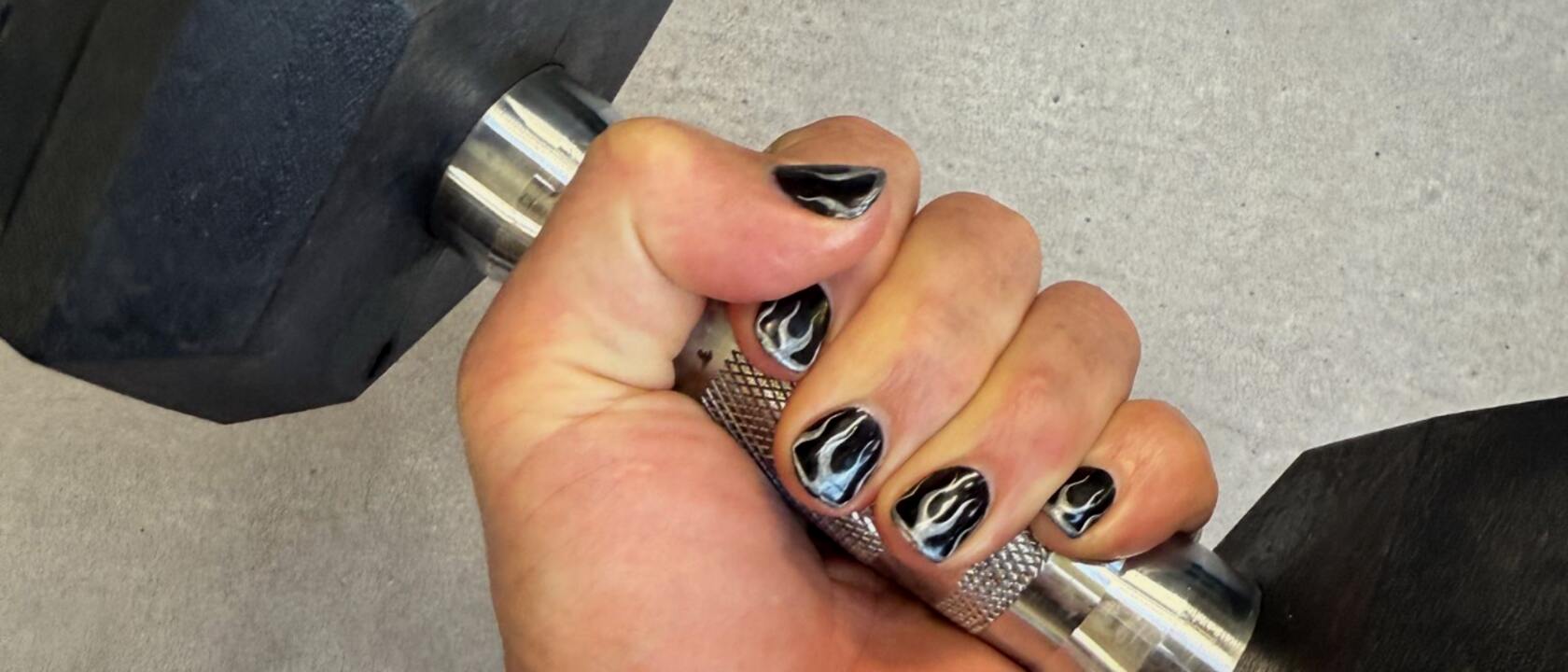A fist gripping a dumbbell, nails painted in black chrome flames