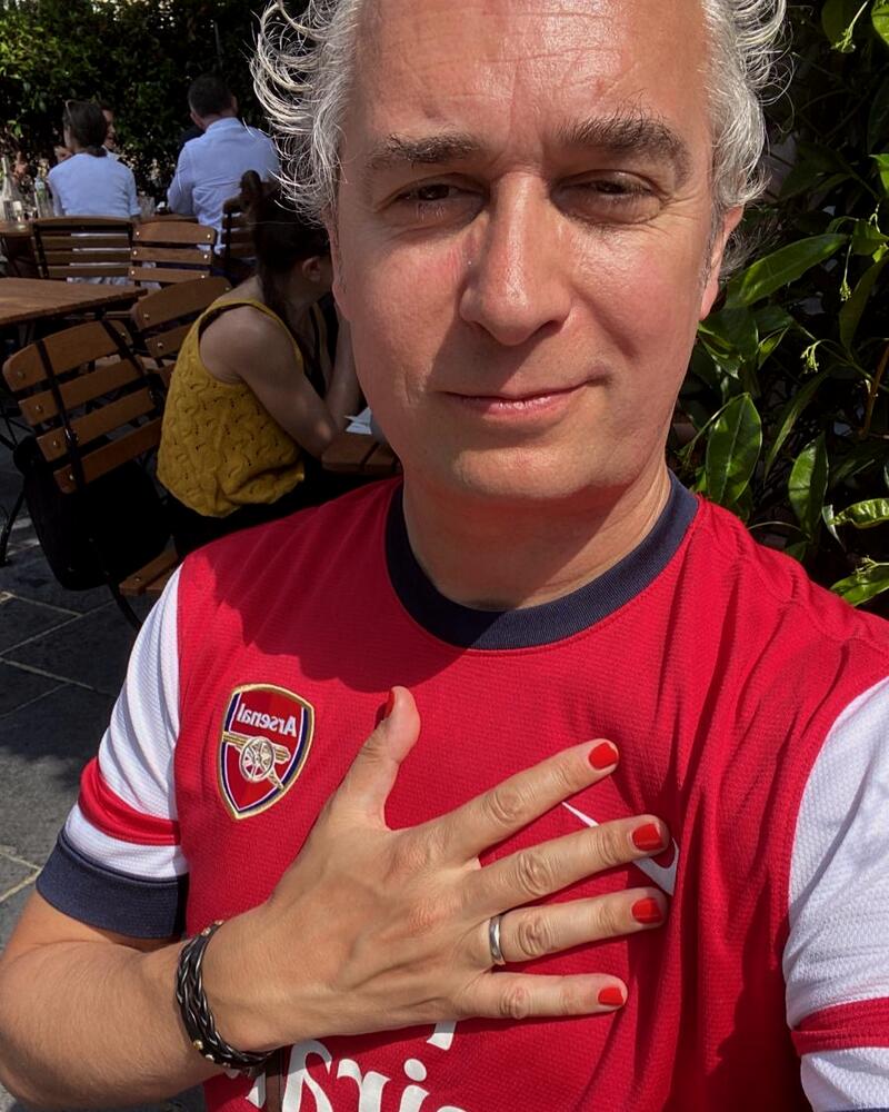 A man in an Arsenal shirt in a pub garden, red painted nails