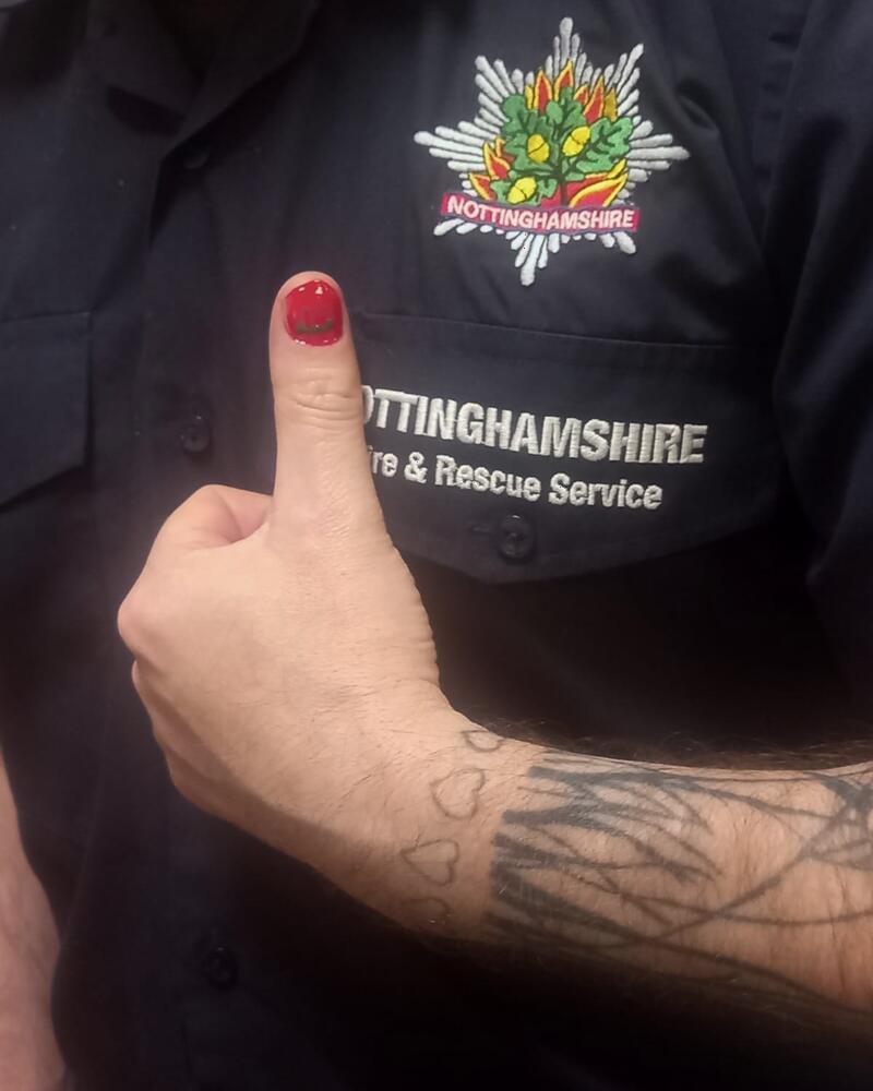 A thumbs up from a tattooed arm, one nail painted red