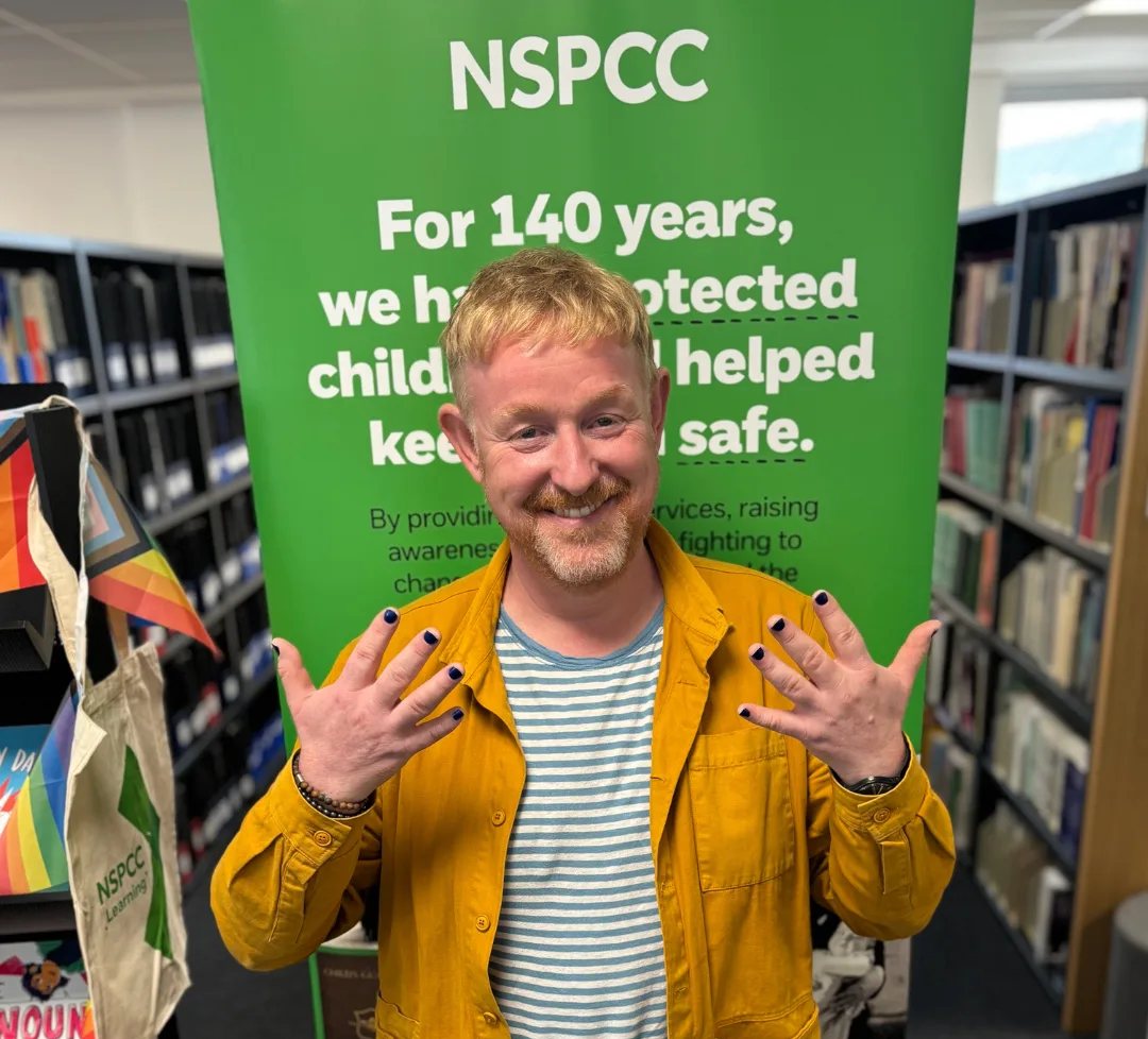 Chris Sherwood at work in an NSPCC office, holding up his painted nails