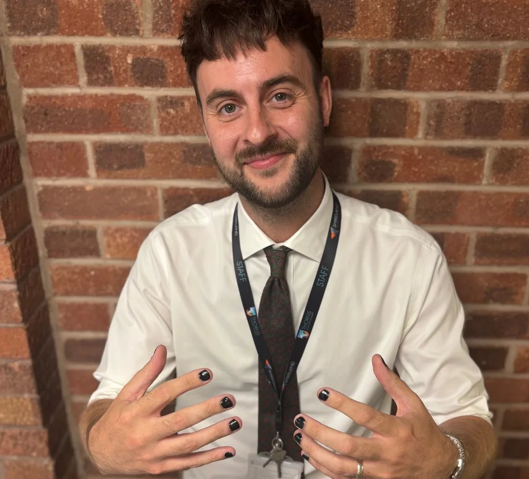 Tom Pell in shirt, tie and work lanyard, holding up his painted nails